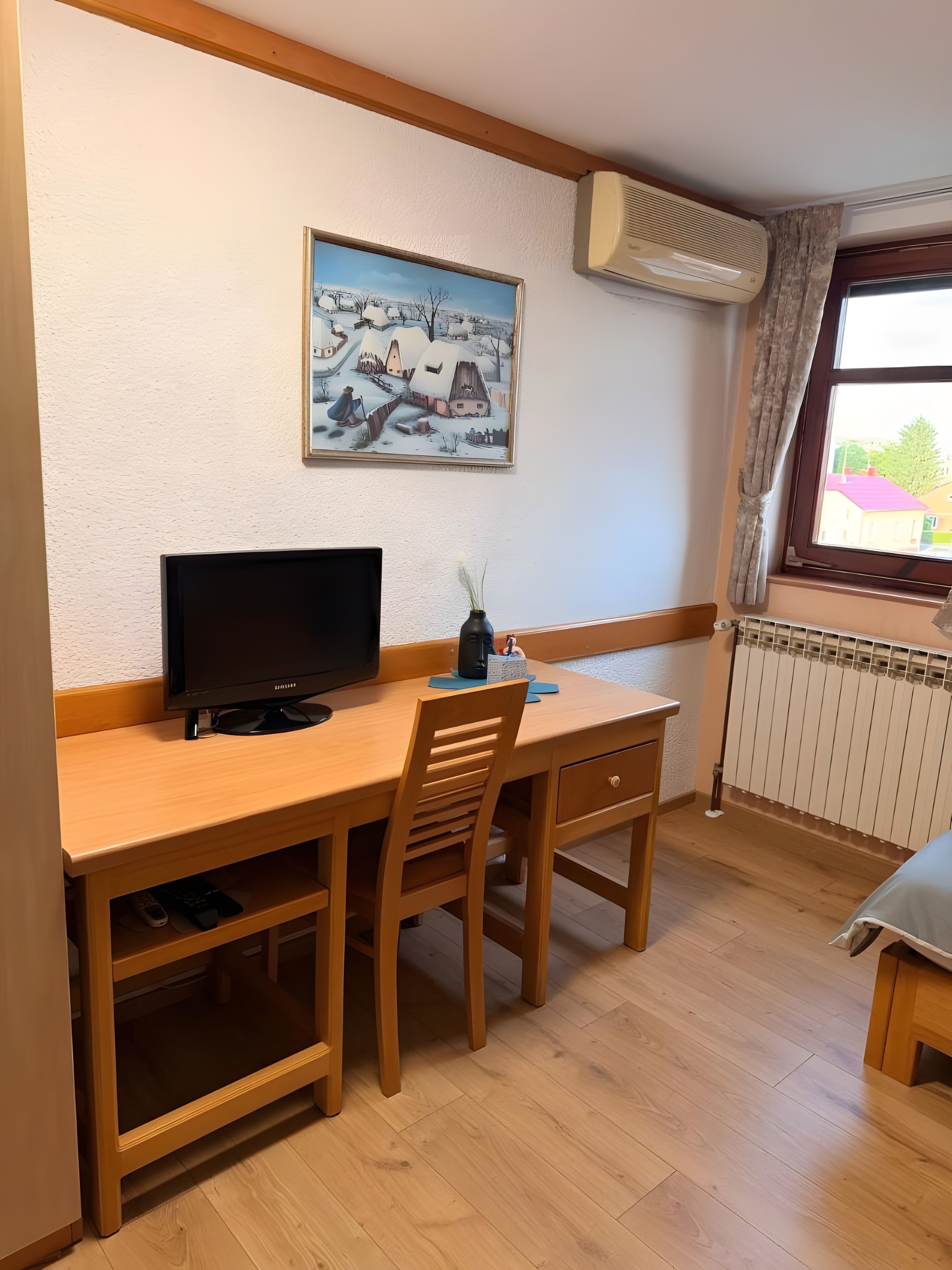 Een kamer met een houten bureau, een televisie, een radiator en een raam met gordijnen.