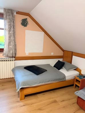 A bedroom with a sloped ceiling, a bed with grey bedding, a radiator, and a small bedside table with a lamp.