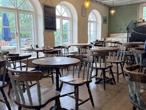 A restaurant interior with multiple wooden tables and chairs, large windows, and a chalkboard menu. - Boutique Lodge (Exeter)