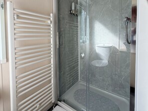 A glass-enclosed shower with a marble floor, a white radiator, and a toilet visible through the glass. - Boutique Lodge (Exeter)