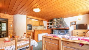 A cozy cabin interior with a stone fireplace, wooden ceiling, and a dining area with a table set for two. - Apartment 'K2' with Mountain View and Private Terrace (Bonneval-sur-Arc)