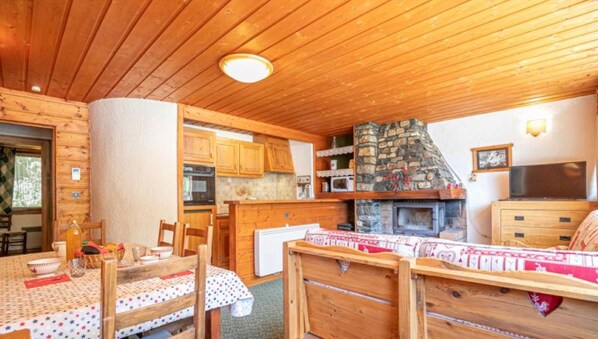 Un accogliente interno di una baita con camino in pietra, soffitto in legno e zona pranzo con tavolo apparecchiato per due.