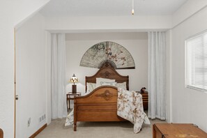 A bedroom with a wooden bed, a bedside table with a lamp, a decorative fan, and a window with blinds. - Lake Thirteen Waterfront Lodge - Fire Pit & Dock (Farwell)
