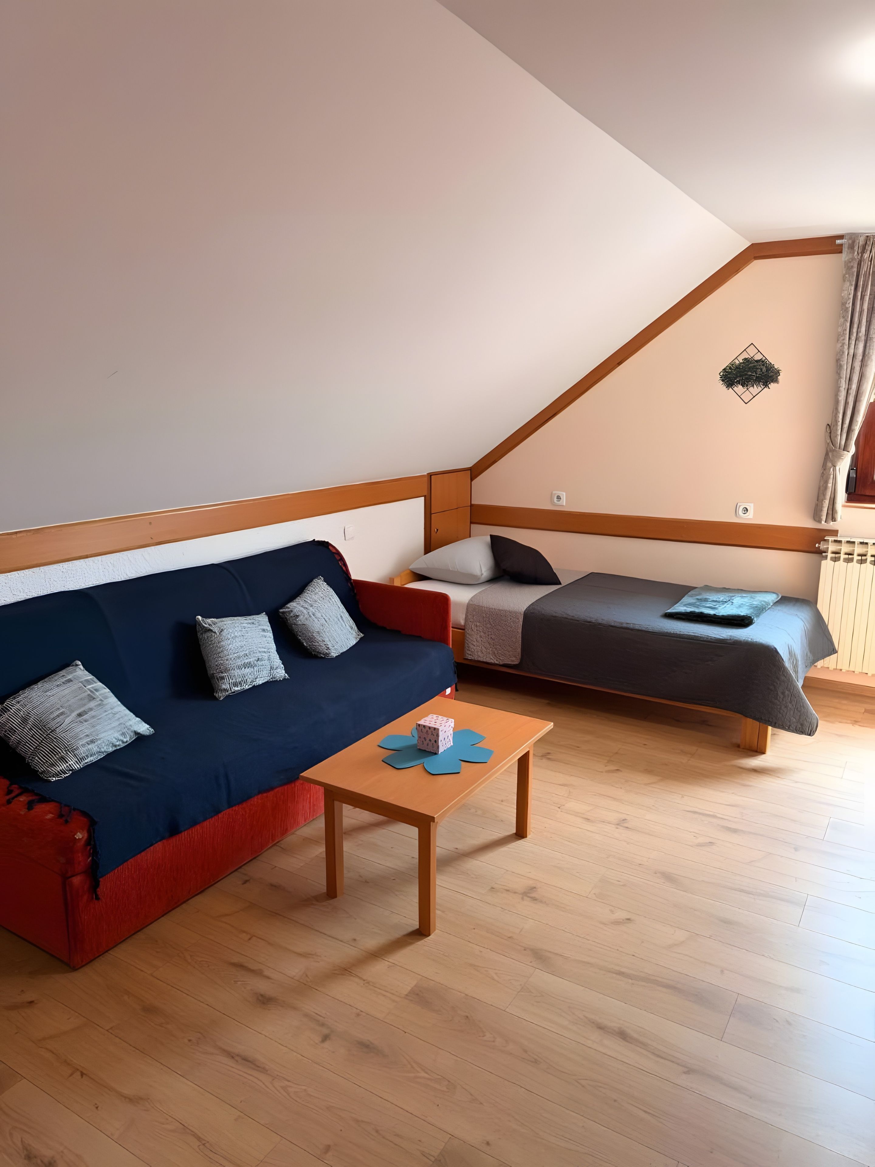 A room with a blue sofa, a wooden coffee table, and a bed with a grey mattress.