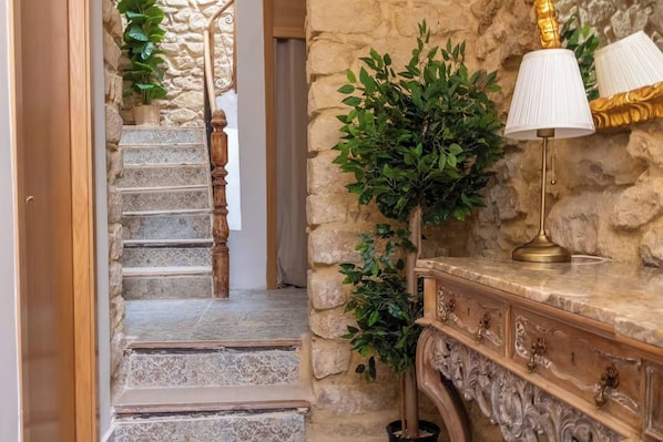 A staircase with stone steps, a wooden handrail, and a wall with a plant and a lamp.