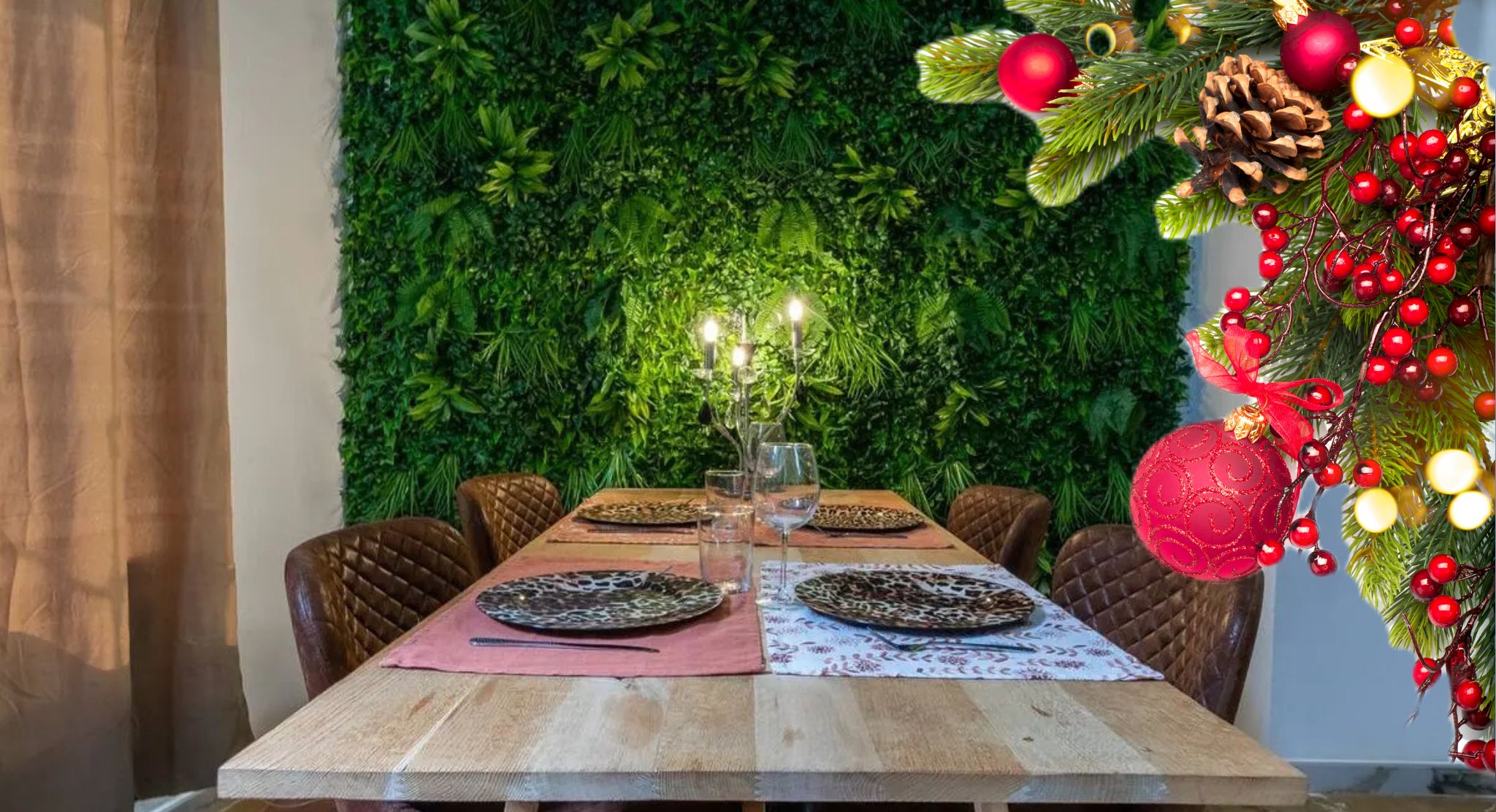 Ein Esstisch ist gedeckt mit Tellern, Gläsern und einer Kerzenarragement, umgeben von Stühlen, vor einer grünen Wand mit einem Weihnachtsbaum rechts.