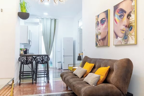 Een woonkamer met een bruine bank, twee gele kussens, en een eethoek met een tafel en stoelen.