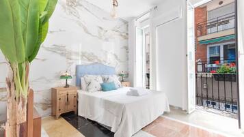 Quarto com cama, mesas de cabeceira, abajur e vista para a varanda.