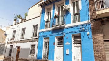 Um edifício com fachada azul, portas brancas e uma varanda com vasos de plantas.