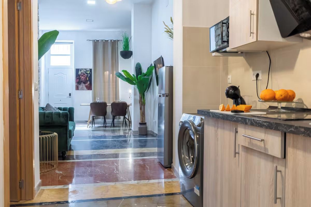 Et moderne køkken med vaskemaskine, et spiseområde med bord og stole, og en stue med sofa.