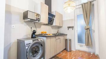 Una cocina compacta con lavadora, horno empotrado y una lámpara colgante.