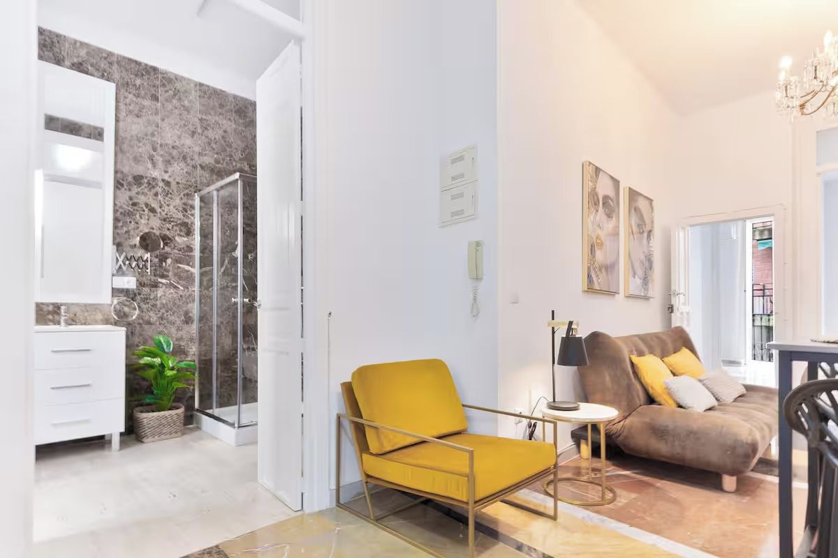 Un salon moderne avec un canapé, un fauteuil jaune et une douche séparée par des parois en verre.