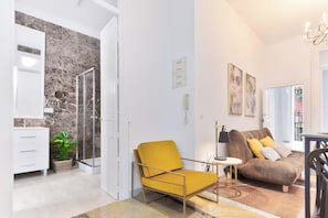 A modern living room with a sofa, a yellow armchair, and a glass-enclosed shower area.