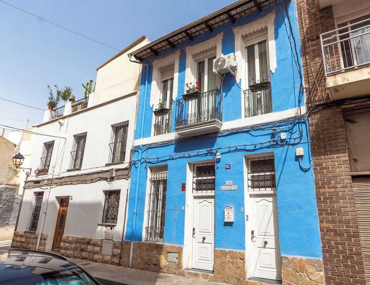 Un bâtiment à la façade bleue, aux portes blanches et doté d’un balcon orné de plantes en pot.