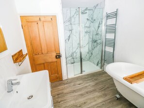 A bathroom with a wooden door, a glass shower enclosure, a white bathtub, and a wooden shelf. - Y Glyn (Borth)