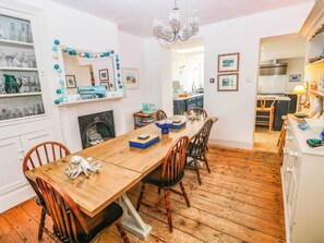 A dining area with a wooden table and chairs, a fireplace, and a kitchen in the background. - Y Glyn (Borth)