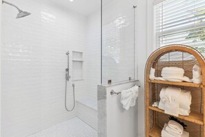 Ein modernes Badezimmer mit weißen Fliesen im U-Bahn-Stil, einer Dusche mit Duschbrause, einer Glaskabine und einem Korbwandschrank mit Handtüchern.