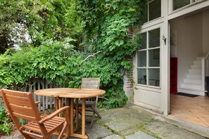 A wooden table and chairs set outdoors, with a brick wall and greenery in the background. - Apartment 'Gîte Du Jardin - Domaine Les Bois' with Wi-Fi (Sixt-sur-Aff)