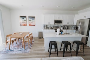 A modern kitchen with white cabinets, a central island, and a dining area with a wooden table and chairs. - Bright 2-Bedroom Home with Mountain Views (Hyrum)
