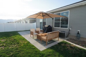 A patio with a table and chairs, a barbecue grill, and a covered umbrella. - Bright 2-Bedroom Home with Mountain Views (Hyrum)