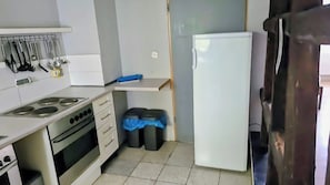 A compact kitchen with a stove, oven, and a refrigerator. There are two trash bins with blue lids. - Large Monteurhaus in Engelsbrand-Grunbach – Up to 14 Guests (Engelsbrand)