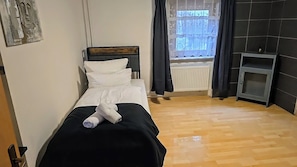 A single bed with white bedding, a black headboard, and a rolled towel on the bed. - Large Monteurhaus in Engelsbrand-Grunbach – Up to 14 Guests (Engelsbrand)