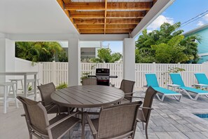 An outdoor patio with a round table and chairs, a grill, and lounge chairs. - 🌴Sandpiper Shores | Heated Pool + Steps to Beach 🌴 (Fort Myers Beach)