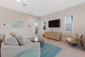 A modern living room with a sofa, a glass coffee table, a TV, and a wooden cabinet. - 🌴Sandpiper Shores | Heated Pool + Steps to Beach 🌴 (Fort Myers Beach)