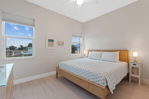A bedroom with a bed, bedside tables, a desk, and windows with views of the outside. - 🌴Sandpiper Shores | Heated Pool + Steps to Beach 🌴 (Fort Myers Beach)