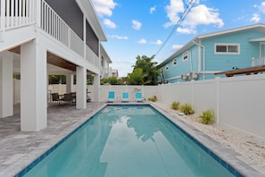 A swimming pool with a white deck, a covered patio area, and a view of neighboring houses. - 🌴Sandpiper Shores | Heated Pool + Steps to Beach 🌴 (Fort Myers Beach)
