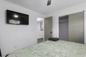 Ein Schlafzimmer mit einem Bett, einem an der Wand montierten Fernseher, einem Kleiderschrank und einer Tür zu einem weiteren Raum.