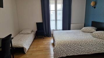 Een slaapkamer met een tweepersoonsbed, een eenpersoonsbed, een stoel en een raam met gordijnen.