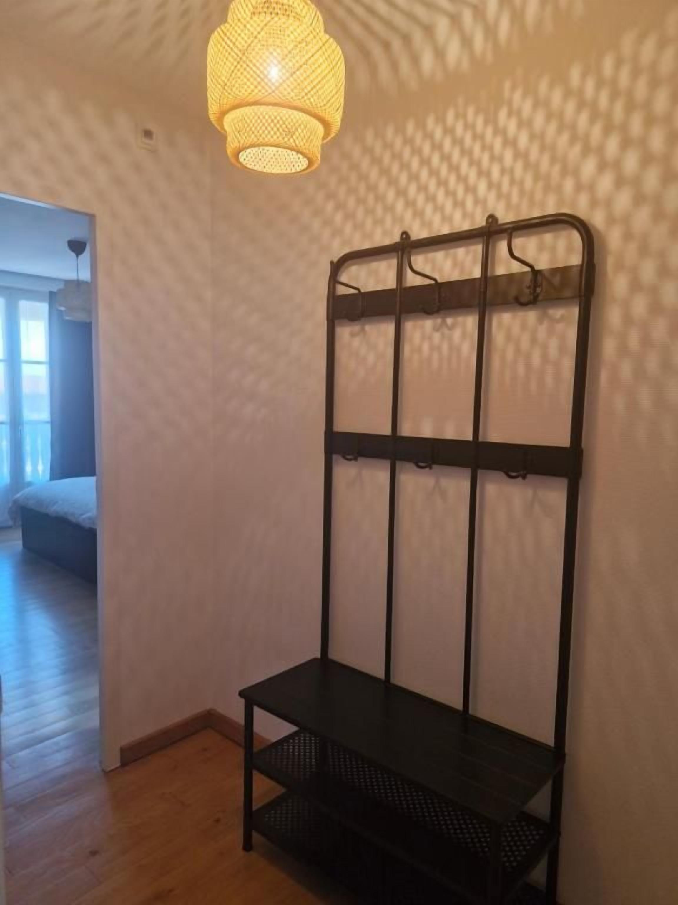 A room with a bed, a hanging light fixture, and a black metal rack with shelves.