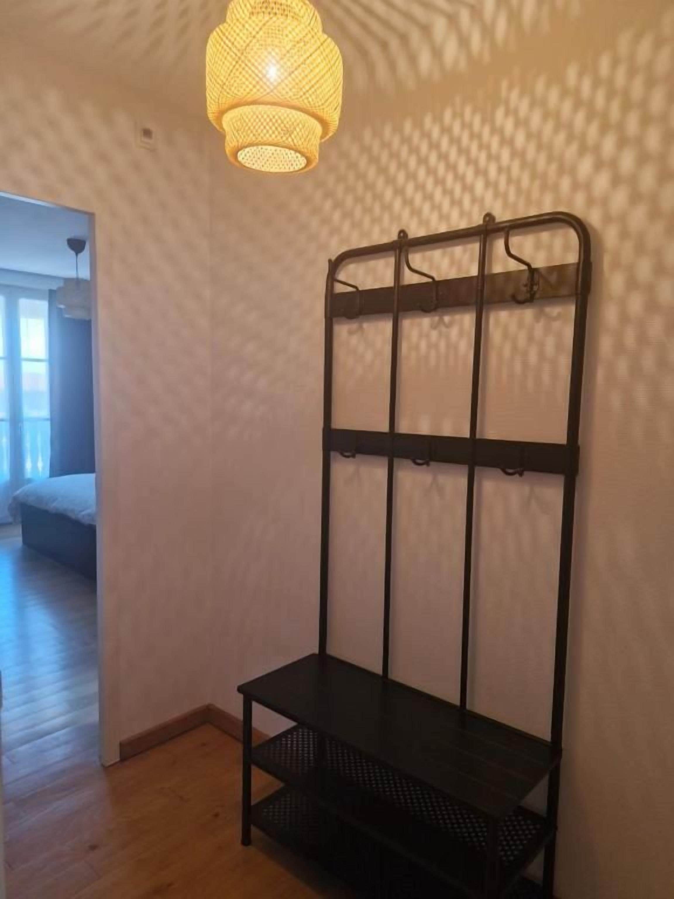 A room with a bed, a hanging light fixture, and a black metal rack with shelves.