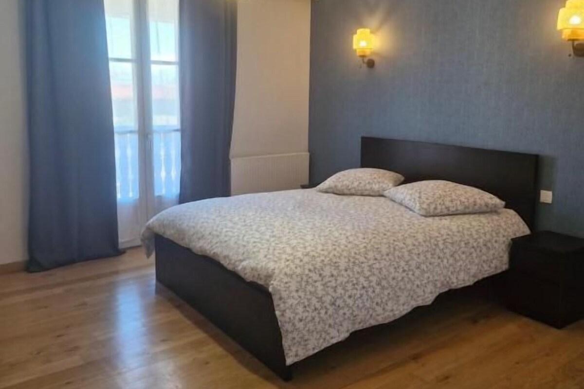 A bedroom with a bed, a nightstand, a window with curtains, and a wall-mounted light fixture.
