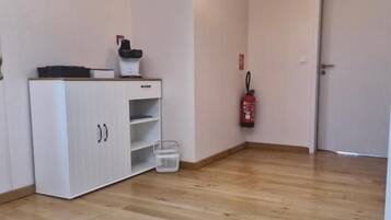 Een kamer met een houten vloer, een wit kastje, een klok, een hanglamp en een deur.