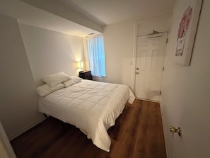 A bedroom with a bed, a nightstand, a lamp, a door, and a window with curtains. - Modern Capitol Hill 1BR - Walk to H Street, Metro & Union Station  Unit 3 (Washington)