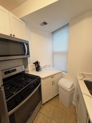 A compact kitchen with a microwave, stove, and white cabinets. - Modern Capitol Hill 1BR - Walk to H Street, Metro & Union Station  Unit 3 (Washington)