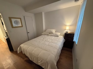 Ein Schlafzimmer mit einem Bett, einem Nachttisch mit Lampe, einer Tür und einem Wandbild.