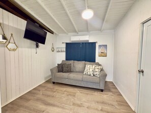 A room with a sofa, a flat-screen TV, a ceiling fan, and a door. - Beachside Escape | Patio, Pool, Pet-Friendly & BBQ (El Combate)