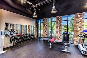 Ein Fitnessstudio mit Trainingsgeräten, großen Fenstern und einer Wand aus Backsteinen.