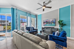 Ein Wohnzimmer mit einer Couch, einem blauen Sessel, einem Couchtisch, einem Fernseher und einem Deckenventilator.