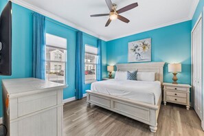 Ein Schlafzimmer mit einem Bett, einem Deckenventilator, einem Nachttisch und einem Fenster mit Vorhängen.