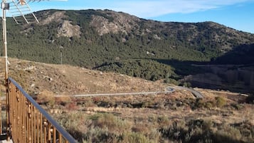 Balcón con barandilla de metal que da a un paisaje montañoso con una carretera y zona boscosa.