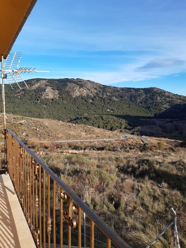 A balcony with a metal railing overlooking a mountainous landscape with a road and forested area.