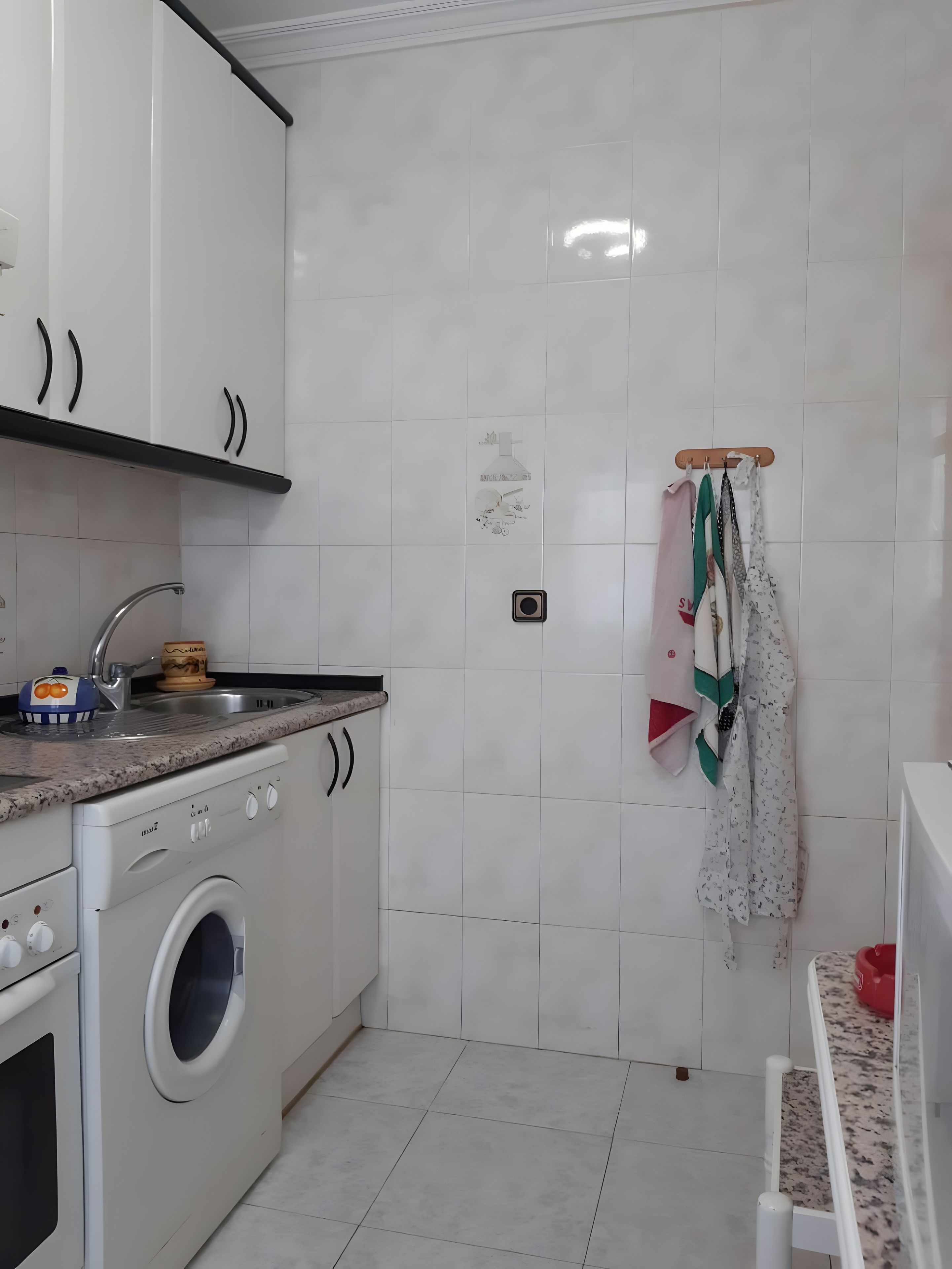 Una cocina con armarios blancos, lavadora, un lavabo y un tendedero con ropa.