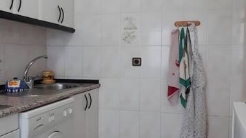 Una cocina con armarios blancos, lavadora, un lavabo y un tendedero con ropa.