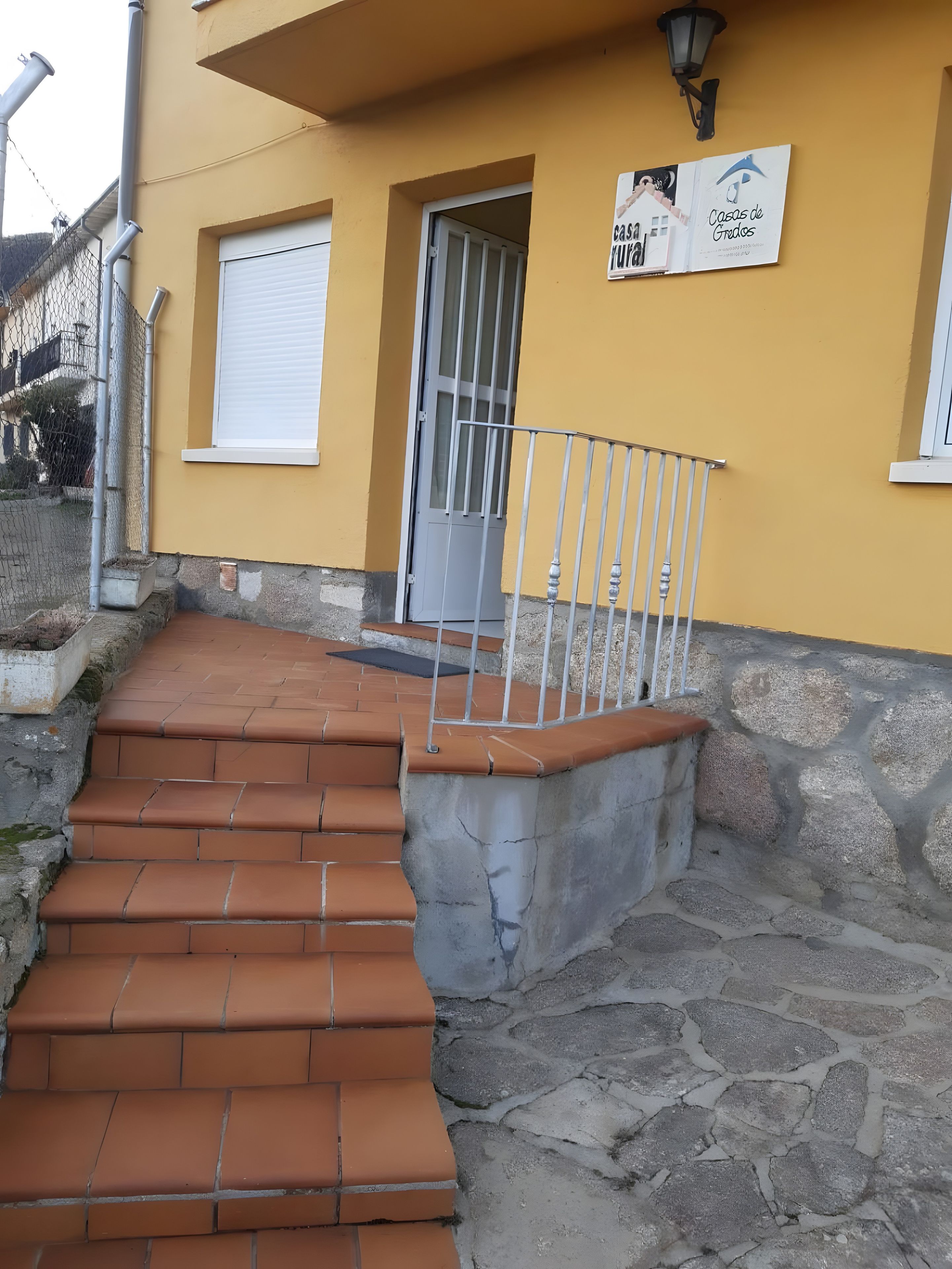 A yellow building with a stone staircase leading to a door, a metal railing, and a sign on the wall.