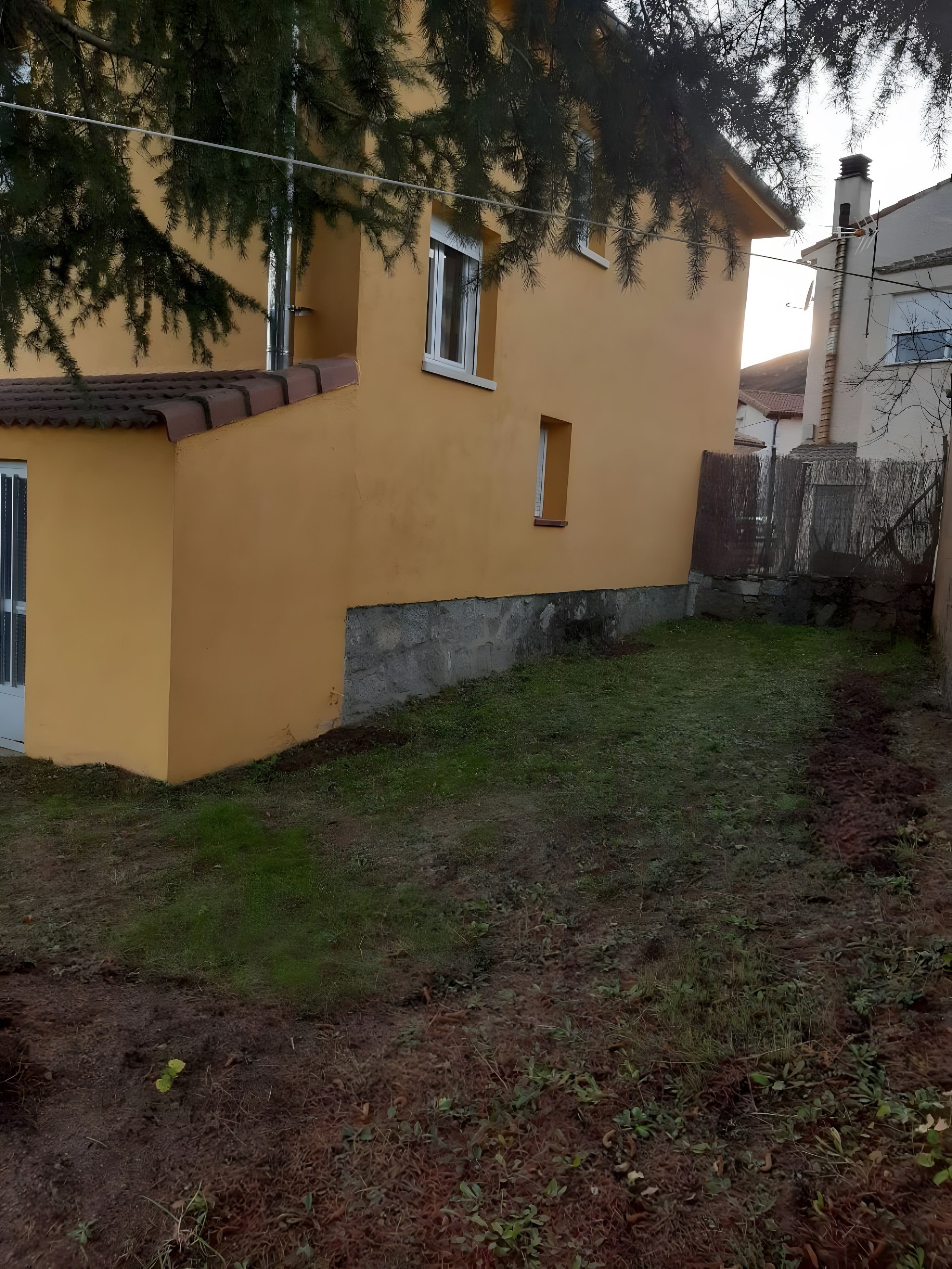 Un bâtiment jaune avec une petite fenêtre et une porte, entouré d’une zone herbeuse et d’un mur en béton.