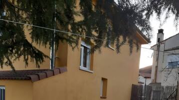 Un bâtiment jaune avec une petite fenêtre et une porte, entouré d’une zone herbeuse et d’un mur en béton.